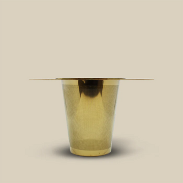A modern round table with a gold cylindrical base displays The Tea Collective’s Tea Infuser Gold—ideal for tea enthusiasts seeking easy brewing. Set against a plain beige background.
